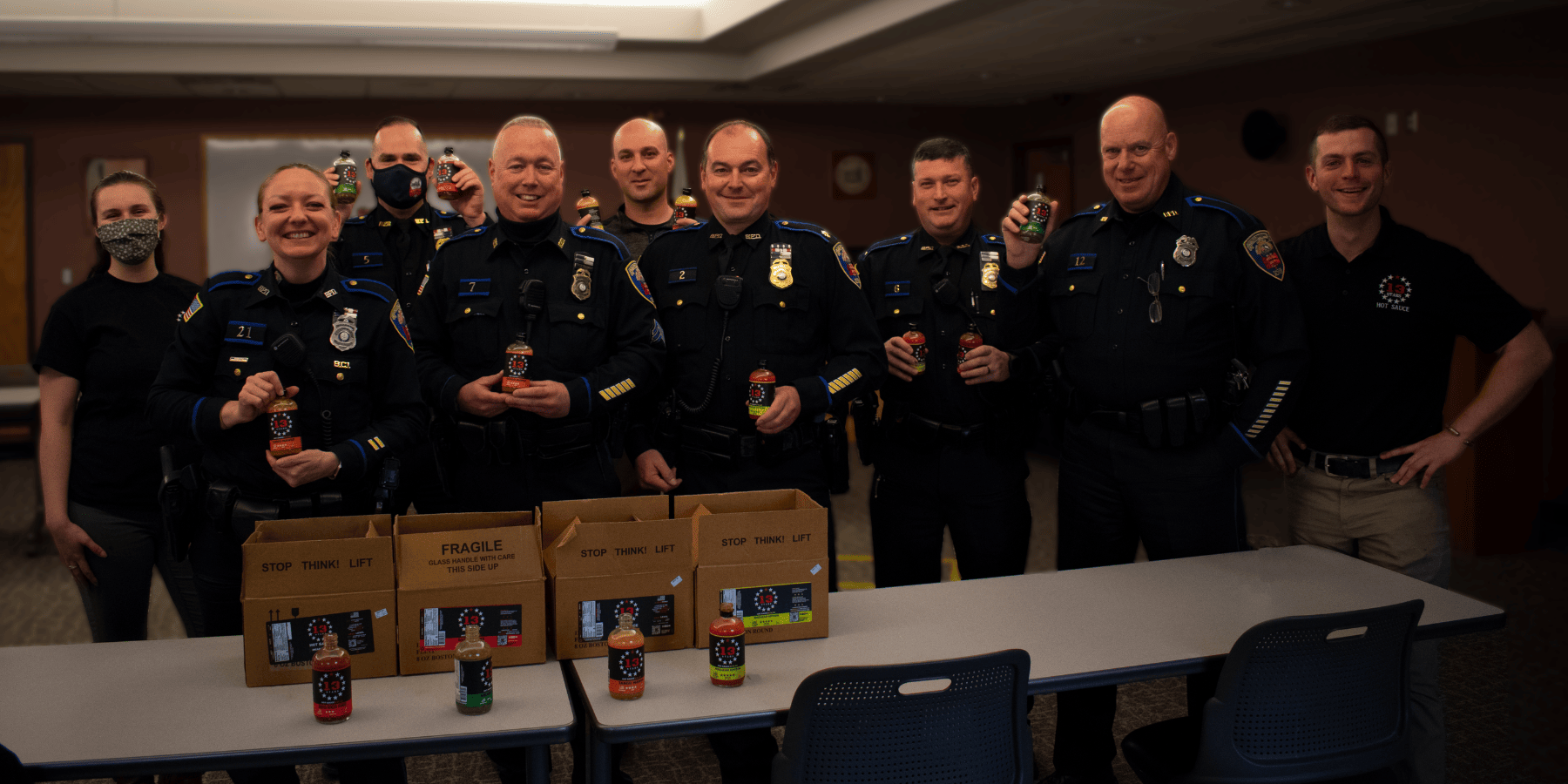 Members of a police department smiling and holding up bottles of 13 Stars Hot Sauce