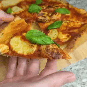 Person holding a slice of pizza with basil leaves on a wooden board